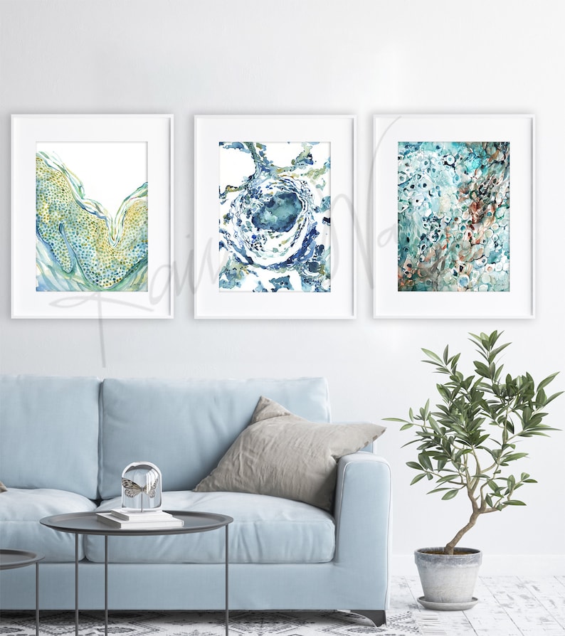 May include: Three abstract watercolor paintings in white frames. The paintings feature blue, green, and gold colors with a swirling, organic pattern.