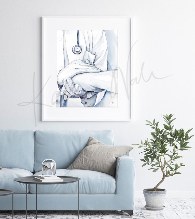 Op de afbeelding: Ingelijste aquarelprint van een arts die de hand van een pati&euml;nt vasthoudt, met een stethoscoop. Het kunstwerk is in blauw- en wittinten. De afbeelding is gemonteerd in een witte lijst en hangt aan een witte muur, wat een rustgevende sfeer cre&euml;ert.