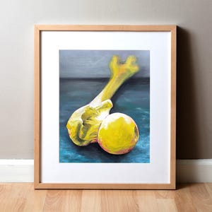 May include: A framed art print featuring a still life composition. The artwork depicts two yellow, organic forms against a teal and gray background. The frame is a light wood color, adding a natural touch to the piece.
