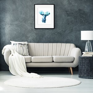May include: A white couch with a white throw blanket and a black and white patterned pillow sits in front of a dark gray wall. A framed print of a blue and white abstract Y-shaped design hangs above the couch. A black side table with a white lamp and a stack of books sits to the right of the couch. A white round rug sits in front of the couch.