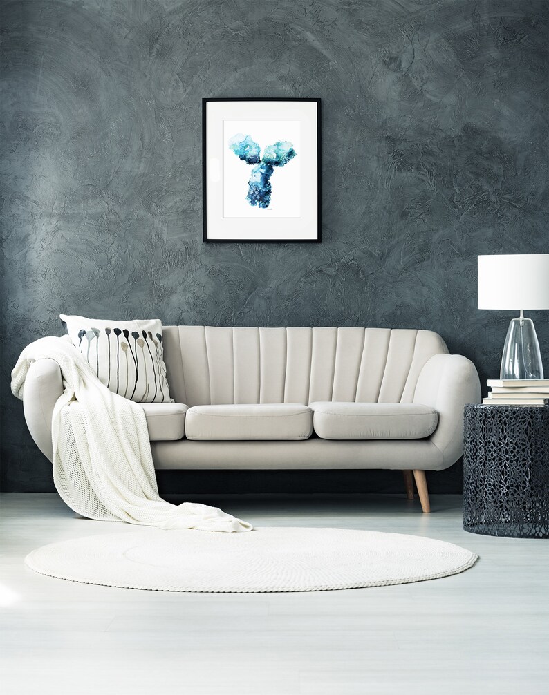 May include: A white couch with a white throw blanket and a black and white patterned pillow sits in front of a dark gray wall. A framed print of a blue and white abstract Y-shaped design hangs above the couch. A black side table with a white lamp and a stack of books sits to the right of the couch. A white round rug sits in front of the couch.