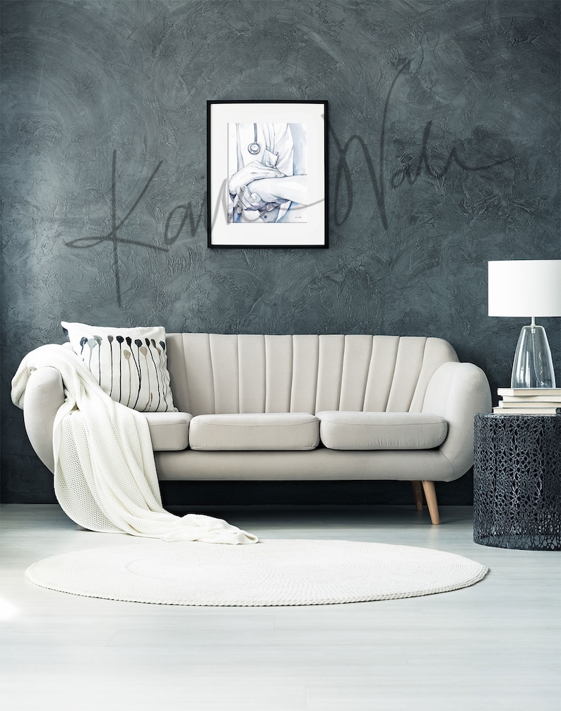 Op de afbeelding: Een ingelijste aquarelprint van de handen van een dokter die een stethoscoop vasthoudt, hangt boven een beige bank. Een witte sprei en een decoratief kussen liggen op de bank. Een wit rond tapijt ligt op de vloer. Een lamp en een bijzettafel bevinden zich rechts.