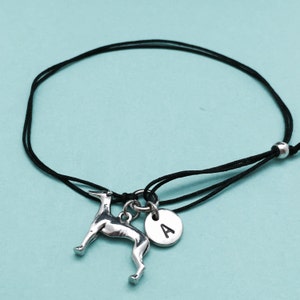May include: Black cord bracelet with a silver charm of a greyhound dog and a silver disc charm with the letter A.