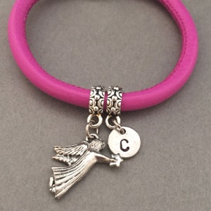 May include: A pink leather bracelet with two silver charm beads. One charm is a silver angel with a star and the other is a silver disc with the letter "C" engraved on it.
