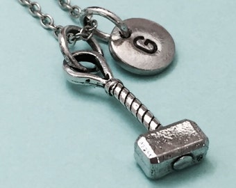 Op de afbeelding: Een zilveren ketting met een kleine zilveren hamerbedel en een zilveren schijfbedel met de letter "G" erop gegraveerd.