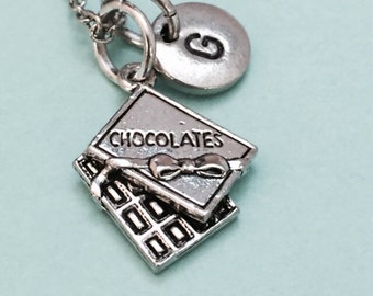 May include: Silver necklace with a chocolate bar charm and a letter G charm. The charm says "Chocolates" on it.