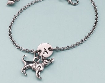 May include: A silver chain bracelet with a charm of a chihuahua and a silver disc with the letter A.