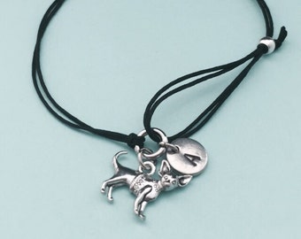May include: Black adjustable cord bracelet with a silver charm of a chihuahua wearing a sweater and a silver charm with the letter A.