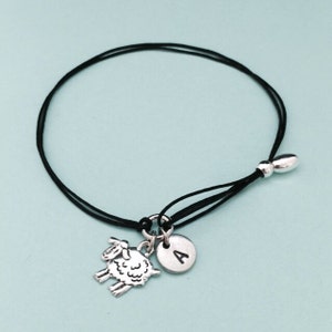 Puede incluir: Un brazalete de cuerda negra con un dije de plata de una oveja y un dije de plata con la letra A.