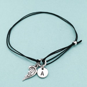 May include: A black string bracelet with a silver angel wing charm and a silver charm with the letter A.