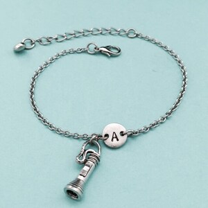 May include: A silver chain bracelet with a charm of a flashlight and a round charm with the letter A.