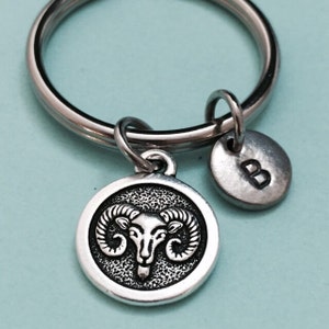 May include: Silver keychain with a round charm featuring a ram's head and a smaller round charm with the letter "B" engraved on it.