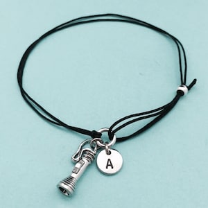 May include: A black cord bracelet with a silver charm of a flashlight and a silver charm with the letter A.