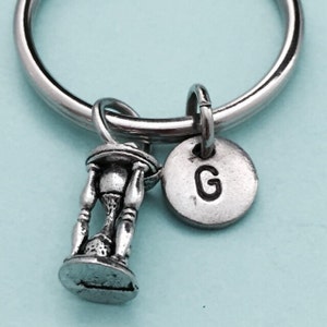 May include: Silver keychain with an hourglass charm and a silver disc charm with the letter G engraved on it.
