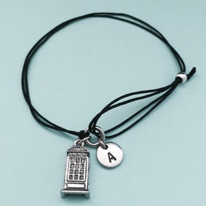May include: A black string bracelet with a silver charm of a London phone booth and a silver charm with the letter A.