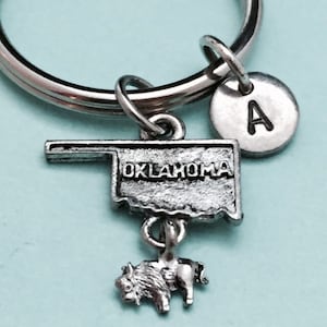 Puede incluir: Llavero de plata con una miniatura del estado de Oklahoma con la palabra "OKLAHOMA" inscrita en ella. Un pequeño amuleto de bisonte de plata cuelga del amuleto del estado. Un amuleto de plata con la letra "A" está unido al anillo del llavero.