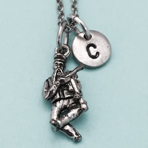 May include: Silver necklace with a charm of a man playing a bagpipe and a silver disc charm with the letter C.