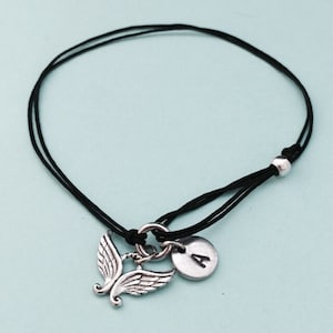 May include: A black string bracelet with a silver angel wing charm and a silver disc charm with the letter "A" on it.