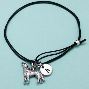 May include: A black cord bracelet with a silver wolf charm and a silver charm with the letter A.