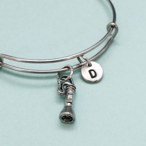 May include: A silver expandable bangle bracelet with a charm of a flashlight and a silver charm with the letter D.