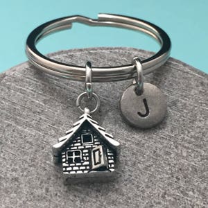May include: Silver keyring with a small house charm and a round charm with the letter J.