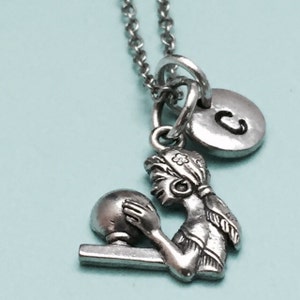 May include: Silver necklace with a charm of a girl holding a bowling ball and a silver charm with the letter C.