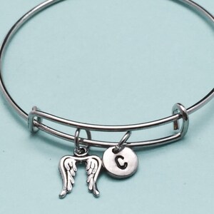 May include: A silver bangle bracelet with a charm of angel wings and a charm with the letter C.