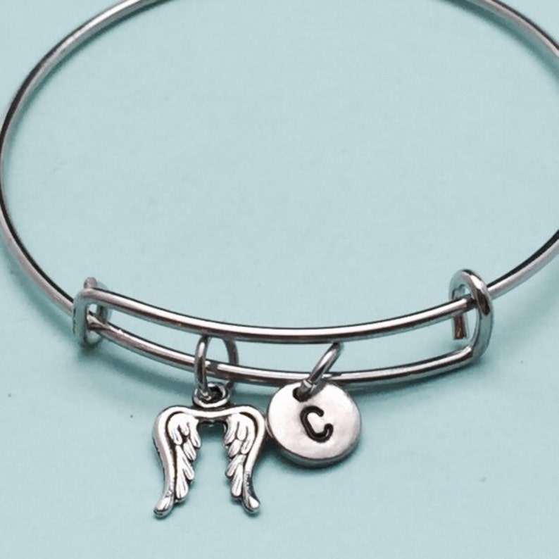 May include: A silver bangle bracelet with a charm of angel wings and a charm with the letter C.
