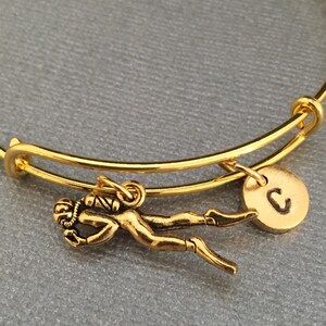 Op de afbeelding: Gouden uitbreidbare armband met een gouden duikerbedel en een gouden bedel met de letter C.