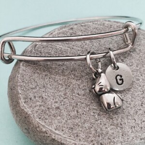 Pode incluir: Um bracelete expansível de prata com um amuleto de gato e um amuleto de prata com a letra G.