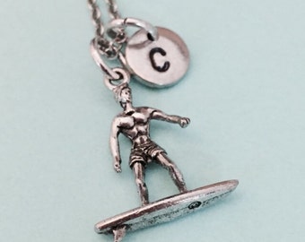 May include: Silver necklace with a surfer charm and a silver disc charm with the letter 'C' on it.