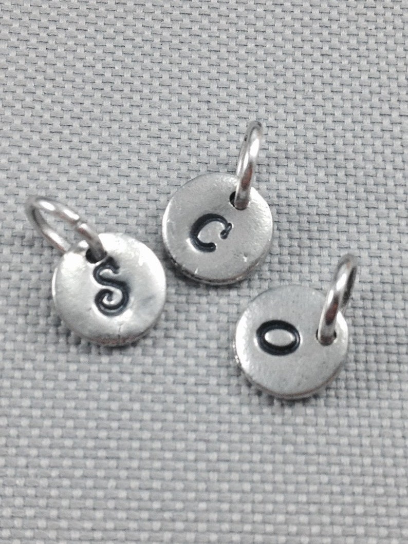 May include: Three silver charms with letter initials C, S, and O. Each charm has a small loop for attaching to a necklace or bracelet.