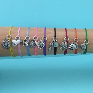 May include: Ten colorful friendship bracelets with different charms, including a sunflower, heart, bee, owl, rose, pineapple, letter A, snowflake, pumpkin, and angel wing.