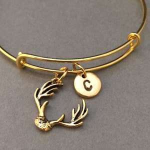 May include: Gold bangle bracelet with a gold antler charm and a gold charm with the letter C.