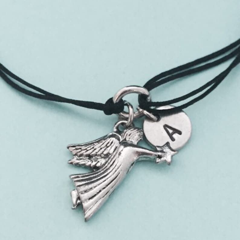 May include: A black cord bracelet with a silver angel charm holding a star and a silver charm with the letter A.