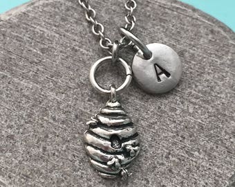 May include: A silver necklace with a beehive charm and a silver charm with the letter A.