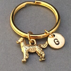 May include: Gold-toned keychain featuring a small golden dog charm, a round charm with the letter "G" engraved on it, and a gold-toned key ring.