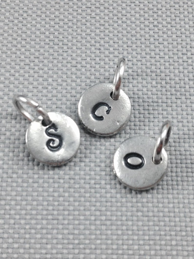 May include: Three silver charms with a loop at the top. Each charm has a letter stamped on the front: C, S, and O.