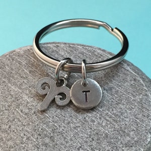 May include: Silver keychain with a zodiac symbol charm and a letter T charm. The zodiac symbol is the Aries symbol.
