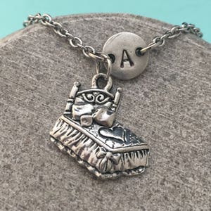 May include: A silver necklace with a bed charm and a round charm with the letter "A" engraved on it.