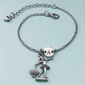 May include: Silver chain bracelet with a charm of a ballerina holding a fan and a silver disc with the letter A.