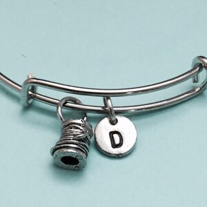 May include: A silver bangle bracelet with a silver spool charm and a silver charm with the letter D.