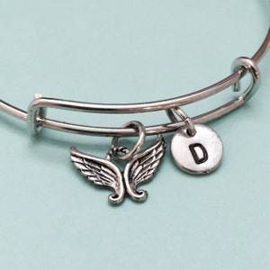 May include: Silver expandable bracelet with a charm of angel wings and a silver disc charm with the letter D.