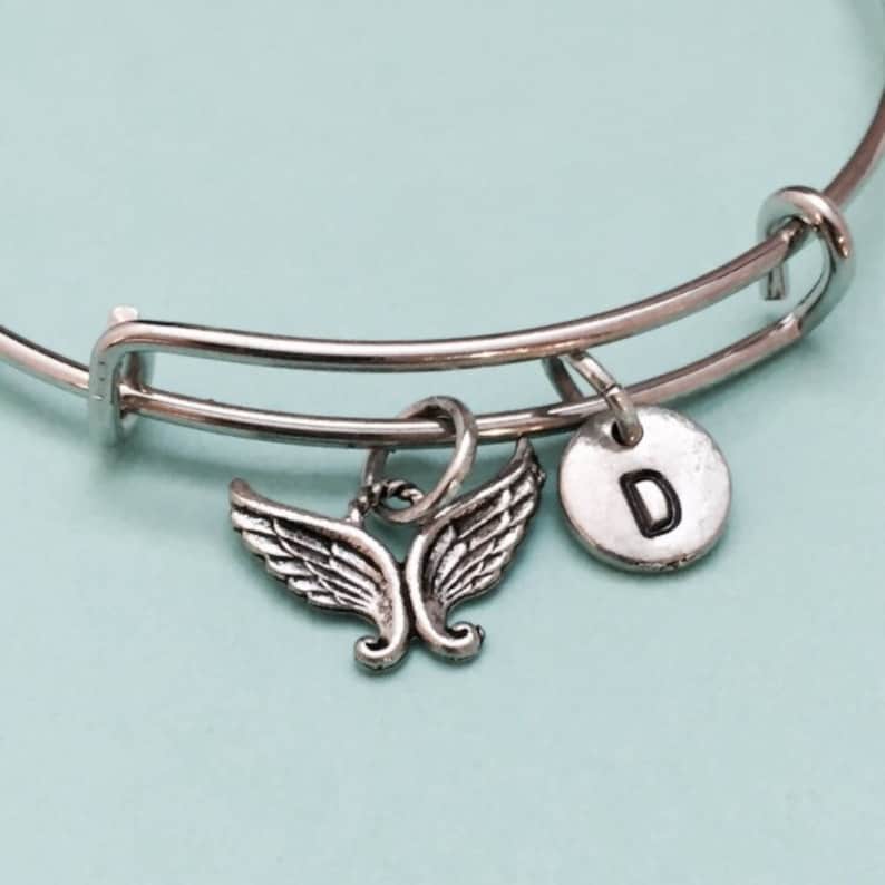 May include: Silver expandable bracelet with a charm of angel wings and a silver disc charm with the letter D.