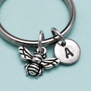 May include: A silver key chain with a small bee charm and a silver disc charm with the letter A engraved on it.
