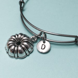 May include: A silver charm bracelet with a cake pan charm and a charm with the letter D.