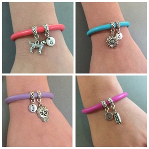 May include: Four colorful leather bracelets with silver charms. The charms include a dog, a sunflower, a skull, and a hot dog. Each bracelet has a silver charm with the letter "C" on it.