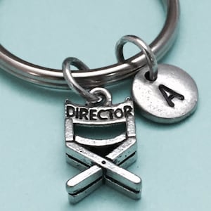 May include: Silver keychain with a director's chair charm and a silver charm with the letter A.