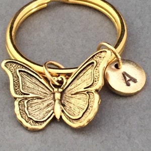 May include: Gold-toned butterfly keychain with a gold-toned initial charm. The initial charm has the letter "A" engraved on it.