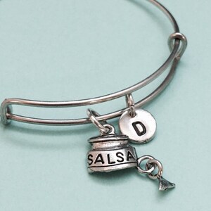 Könnte beinhalten: Silbernes Armband mit einem Salsa-Anhänger, einem Anhänger mit dem Buchstaben D und einem kleinen Anhänger in Form einer Salatschüssel.